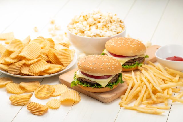 おいしいハンバーガー、フライドポテト、ポップコーン、ポテトチップスが白くて素朴な木のテーブルに並べられている。